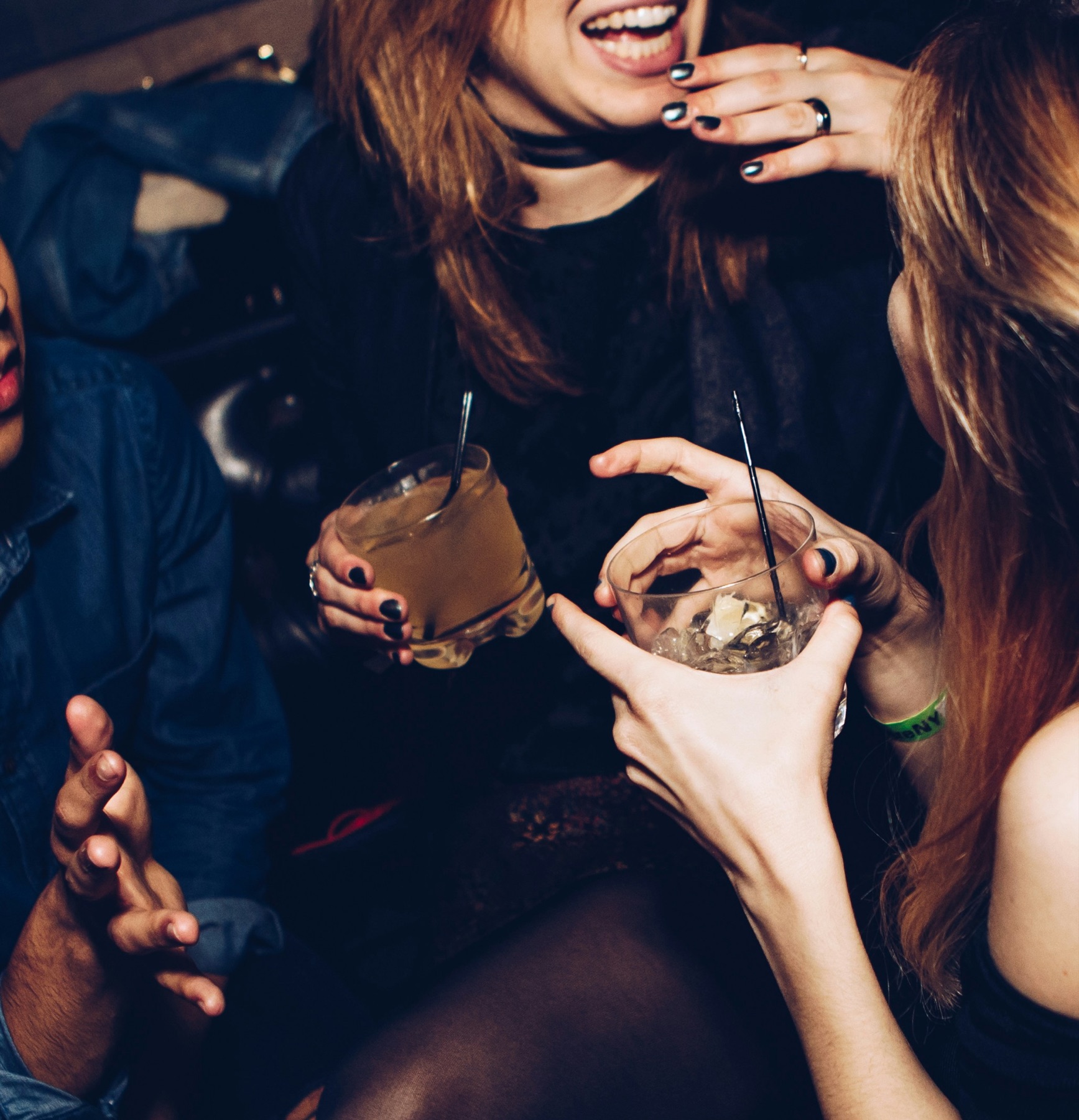 Guests with drinks in hand at a night, one mid-laugh, warm light, no one looking at the camera.
